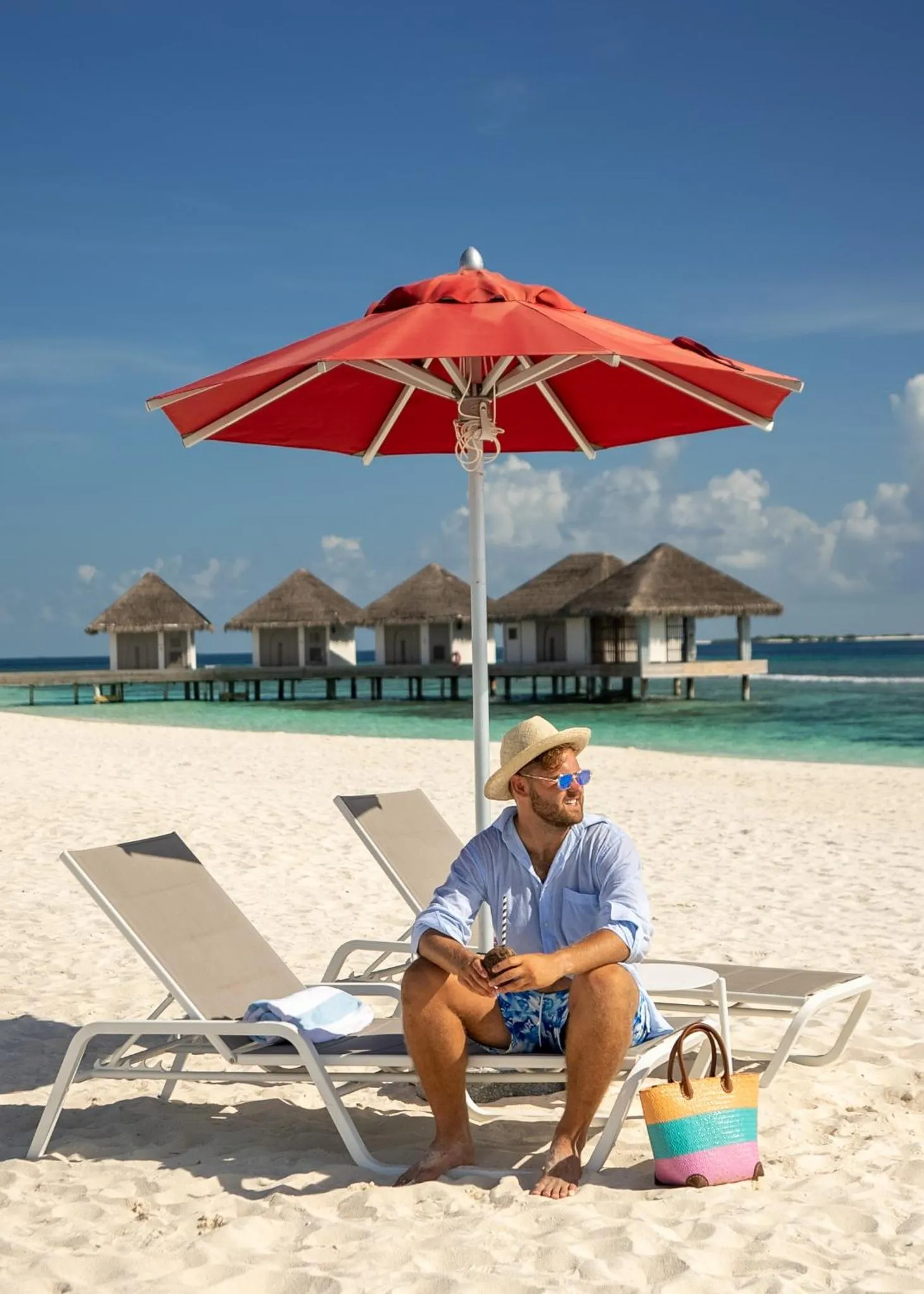 Un homme se repose sur une chaise longue sur une plage de sable blanc.