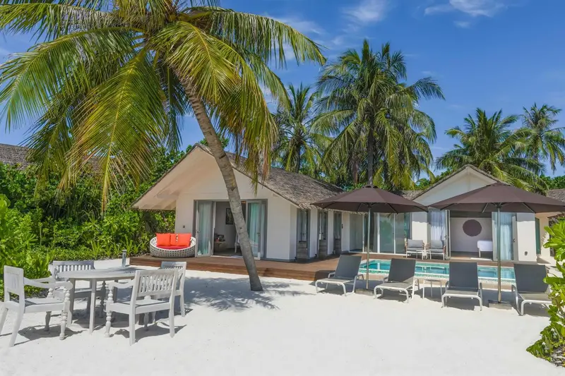 Vue d'une plage de sable blanc avec des bungalows et des palmiers.