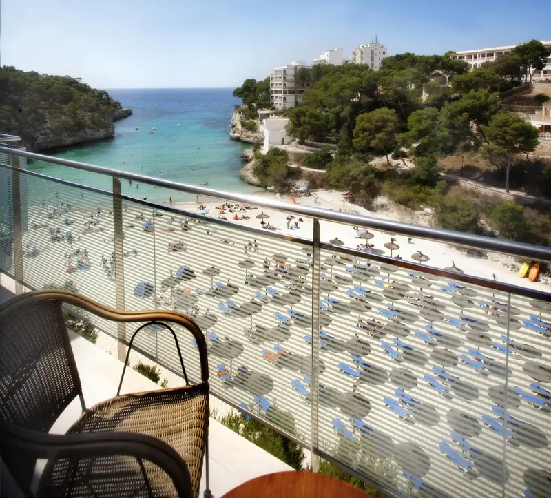Vue d'une plage ensoleillée depuis un balcon avec mobilier d'extérieur.
