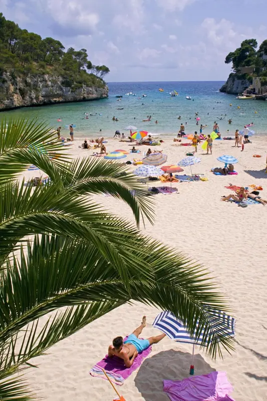 Une plage de sable fin bordée d'une eau turquoise et de parasols colorés.