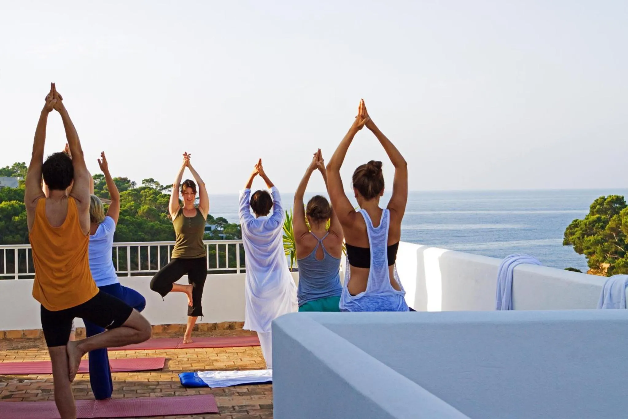 Un groupe de personnes pratique le yoga sur une terrasse ensoleillée avec vue sur la mer.
