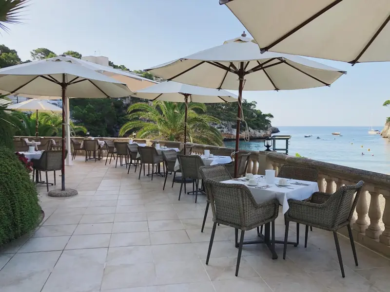 Terrasse ombragée avec tables dressées en vue sur la mer.