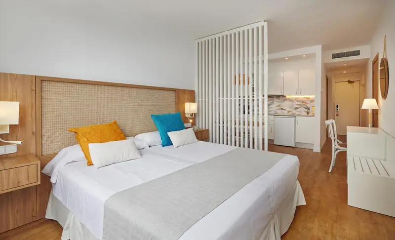Chambre lumineuse avec un grand lit et un espace cuisine ouvert.