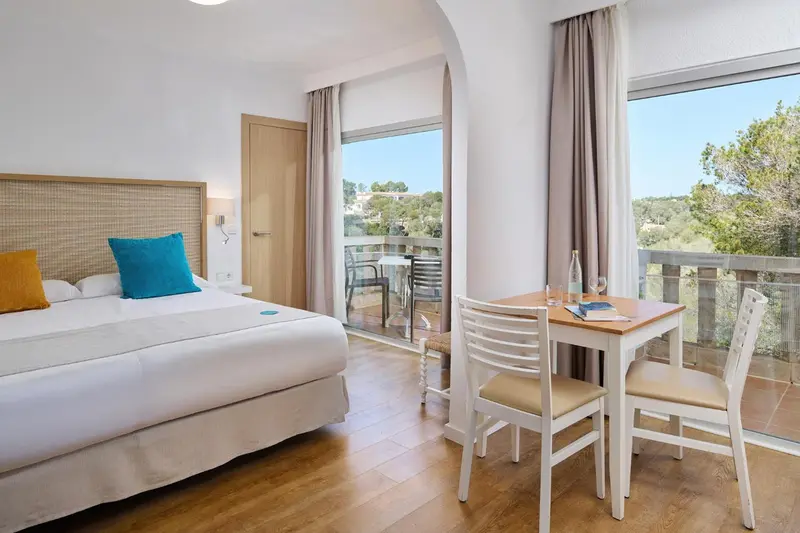Chambre lumineuse avec un lit et un coin repas donnant sur une terrasse.