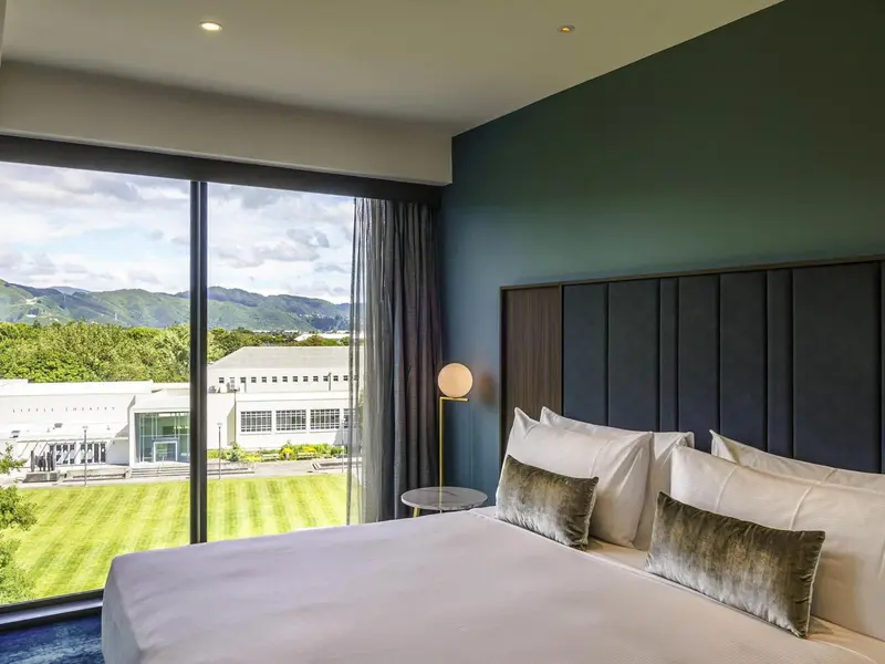 Une chambre lumineuse avec un grand lit donnant sur un paysage verdoyant.