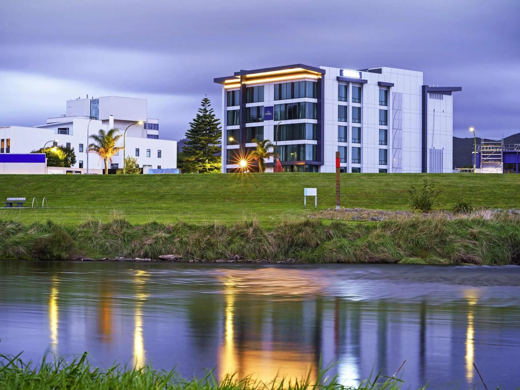 Bâtiment moderne éclairé au crépuscule, reflété dans l'eau calme.