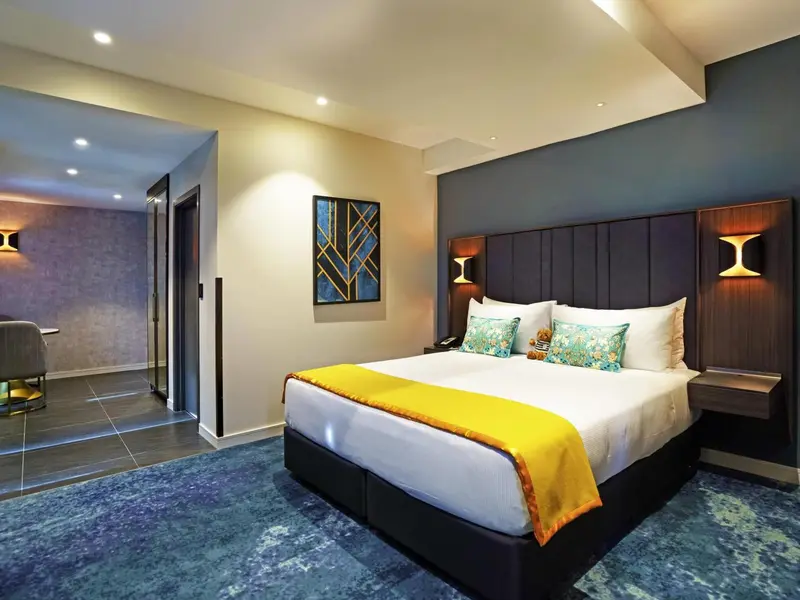 Une chambre lumineuse avec un grand lit recouvert d'une couverture jaune et de coussins décoratifs.
