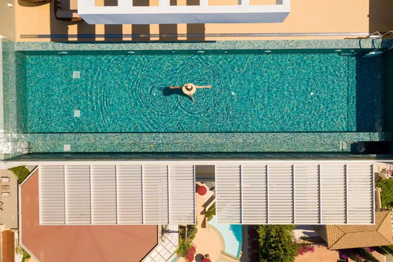 Vue aérienne d'une piscine rectangulaire turquoise avec une personne nageant au centre.