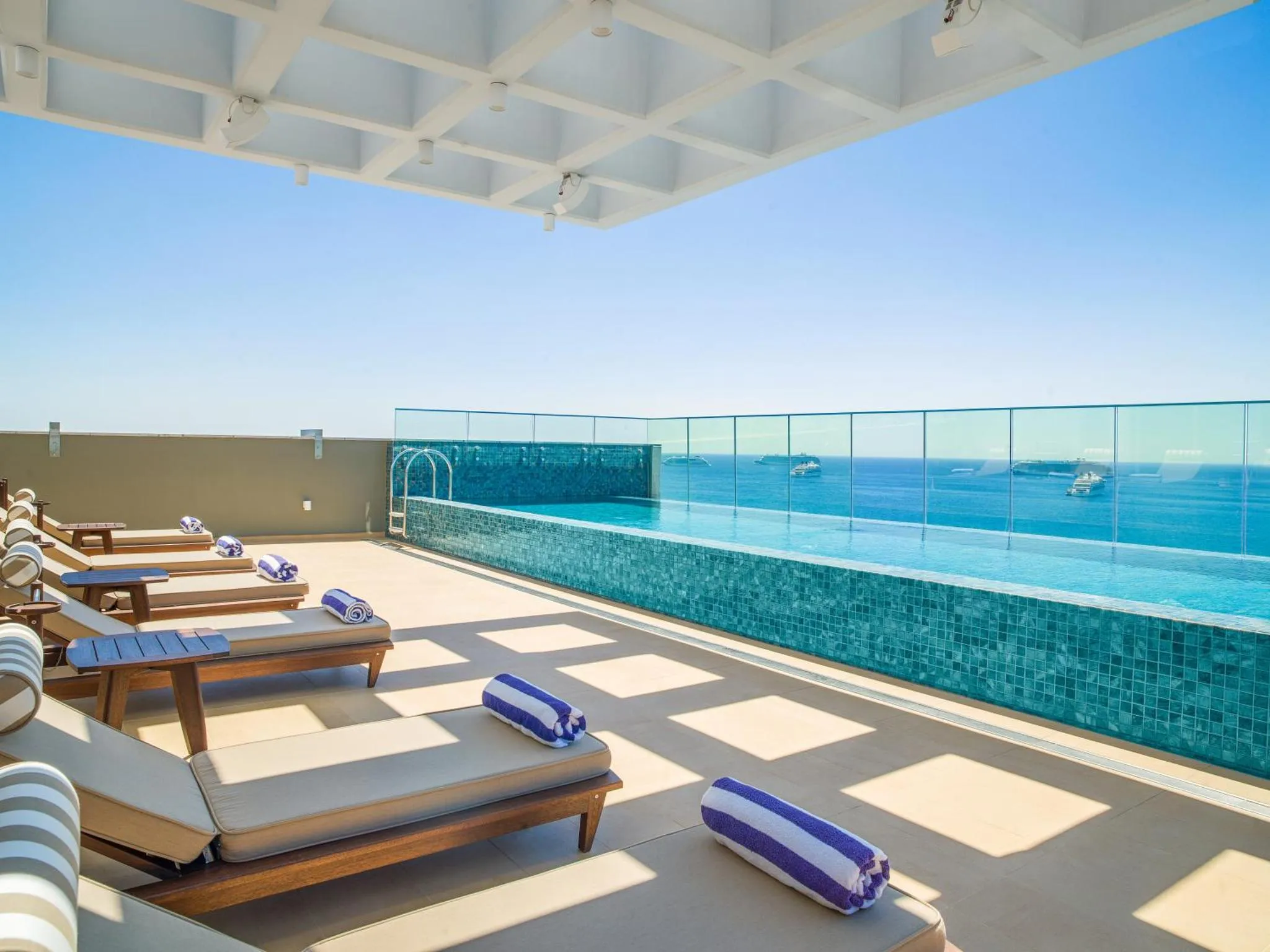 Terrasse avec transats et piscine à débordement donnant sur la mer.