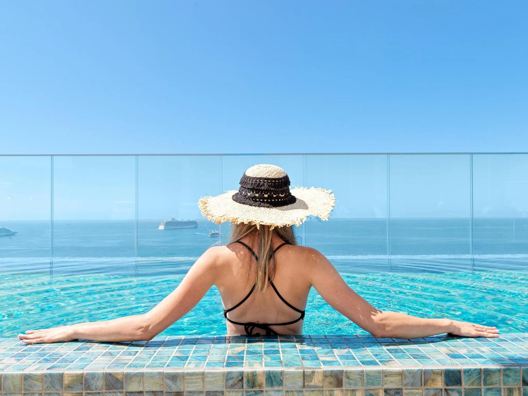 Une femme se détend au bord d'une piscine à débordement avec vue sur la mer.