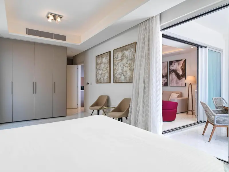 Une chambre lumineuse s'ouvre sur une terrasse avec des fauteuils.