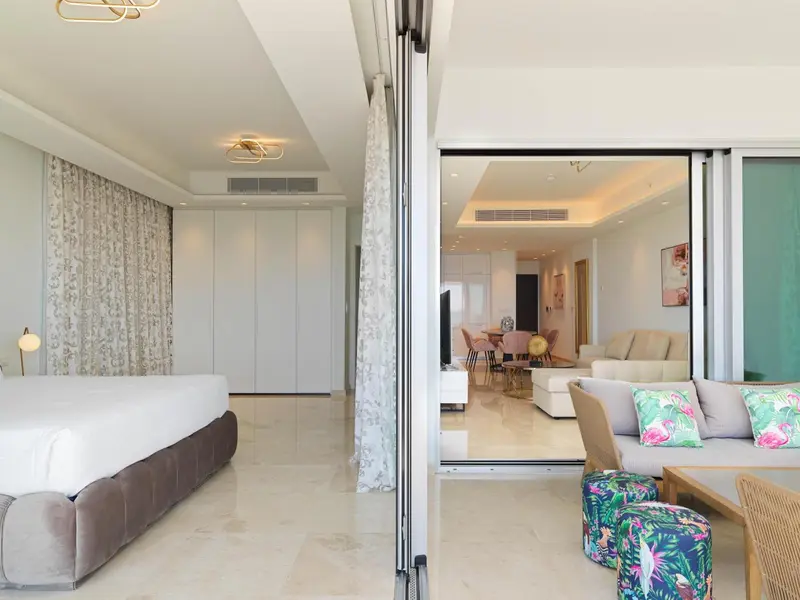 Une chambre lumineuse s'ouvre sur un espace de vie avec canapés et table à manger.