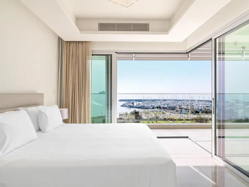 Une chambre lumineuse avec un grand lit donnant sur une vue mer et un port de plaisance.