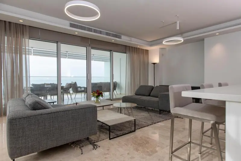 Un salon moderne avec canapés et table basse, donnant sur une terrasse et la mer.