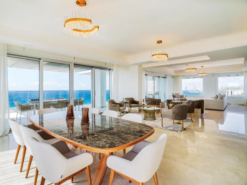 Une grande salle à manger lumineuse avec une table dressée et de larges baies vitrées donnant sur la mer.