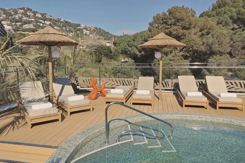 Terrasse avec transats et jacuzzi offrant une vue sur la végétation et la mer.