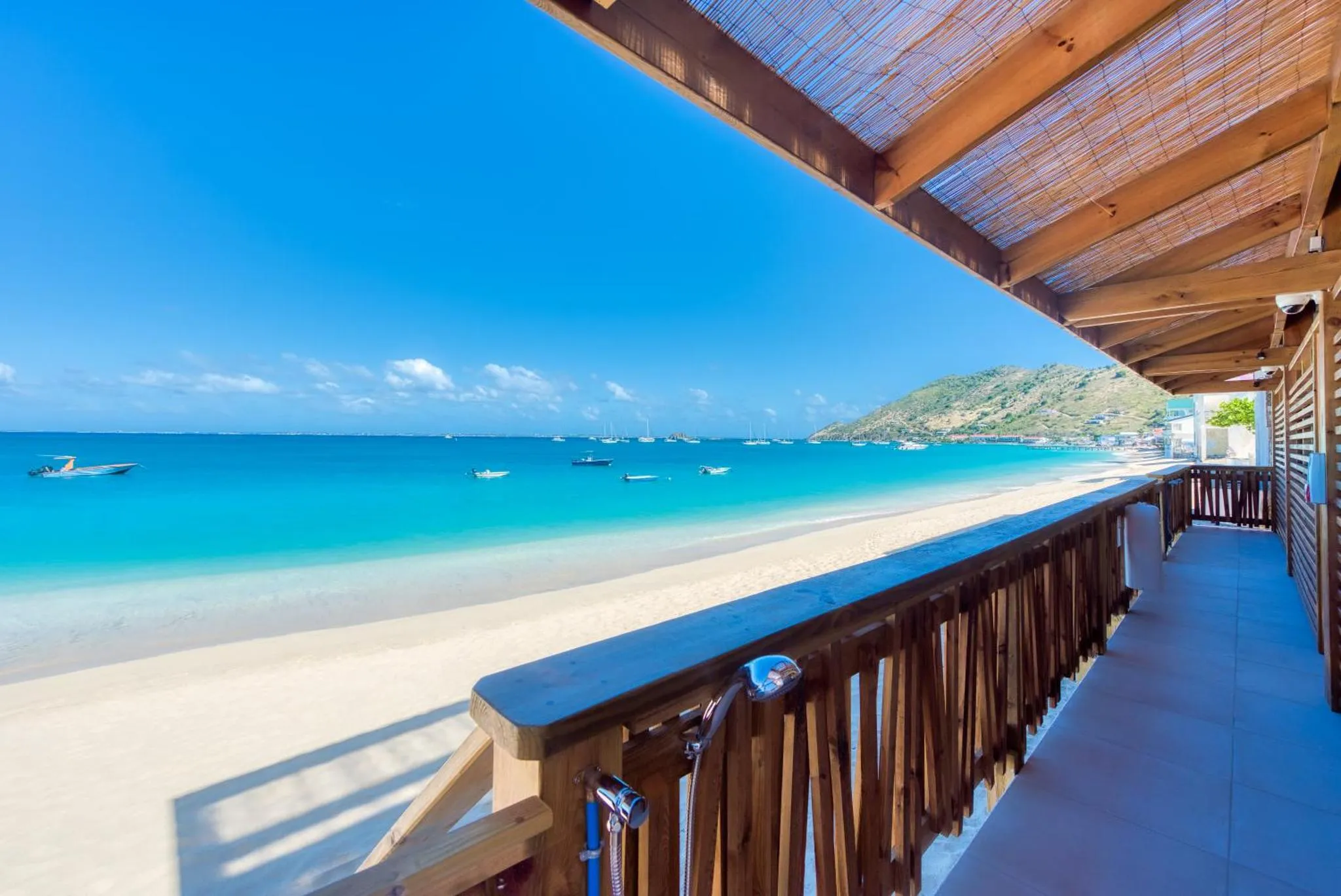 Vue sur une plage de sable fin et une mer turquoise depuis une terrasse ombragée.