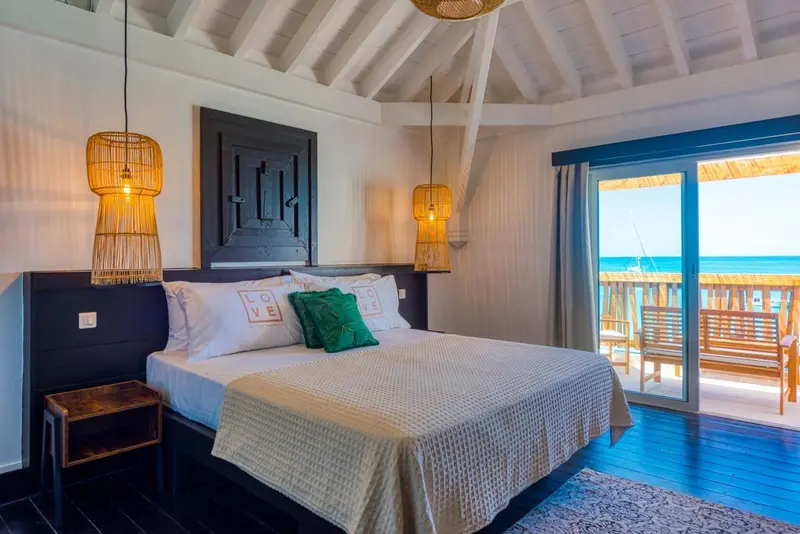 Une chambre lumineuse avec un grand lit donnant sur une terrasse et la mer.