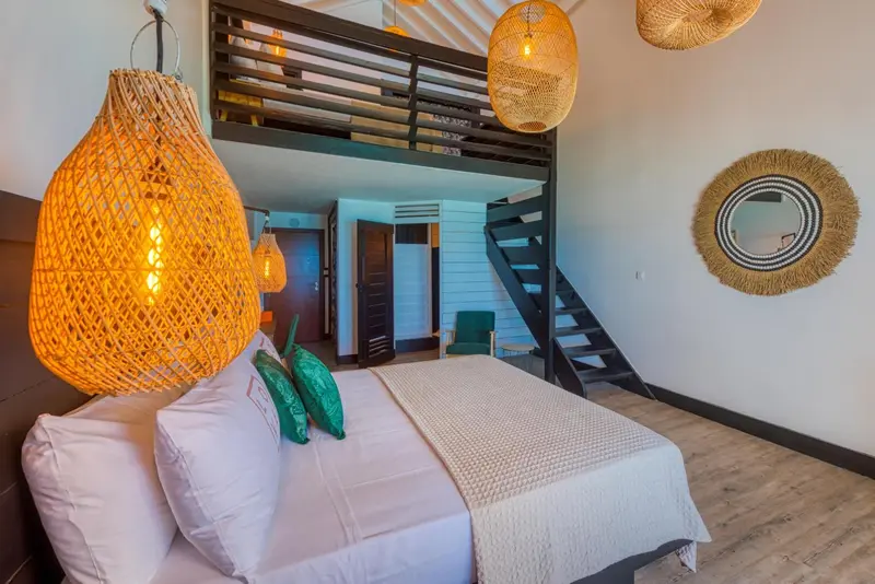 Une chambre lumineuse avec un lit recouvert d'une courtepointe blanche et des suspensions en fibres naturelles.