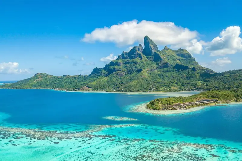Vue aérienne d'une île tropicale avec une montagne verdoyante et une eau turquoise.