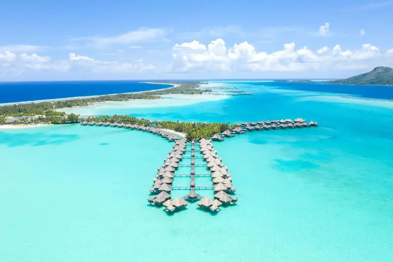 Vue aérienne d'un complexe hôtelier sur pilotis dans une lagune turquoise.