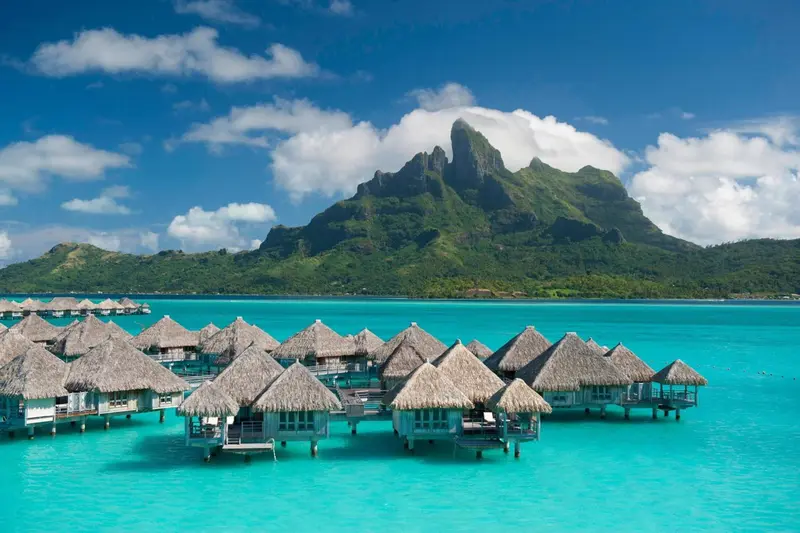 Vue aérienne d'un ensemble de bungalows sur pilotis dans une eau turquoise.
