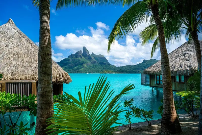 Des bungalows sur pilotis bordent une eau turquoise sous un ciel bleu nuageux.