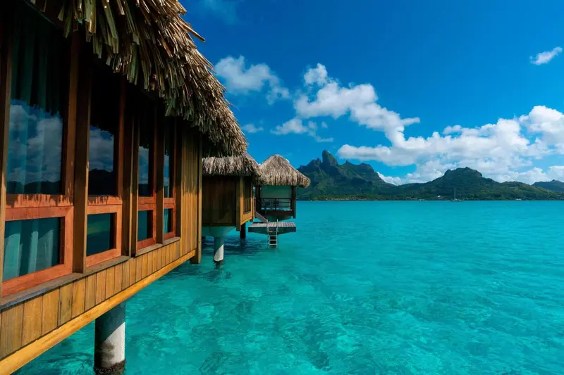 Maisons sur pilotis au-dessus d'une eau turquoise sous un ciel bleu nuageux.