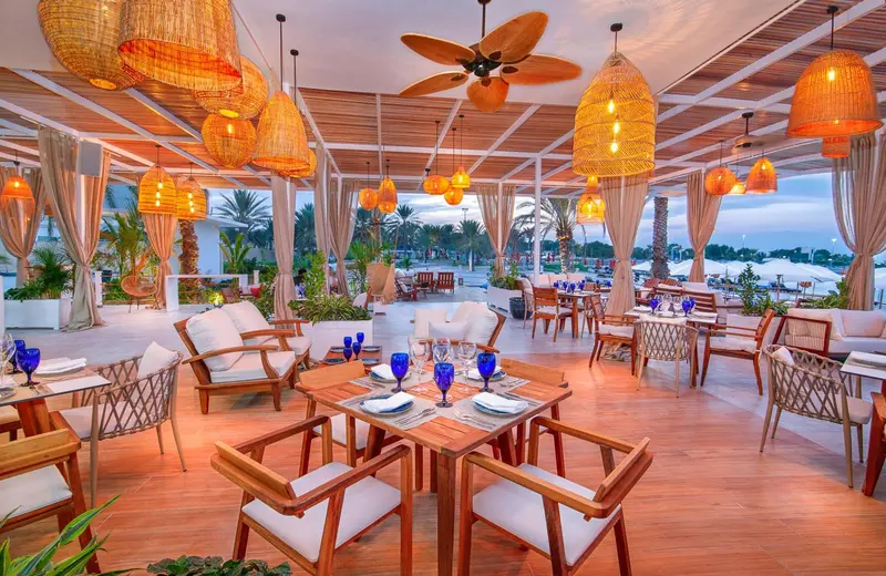 Une salle à manger extérieure avec des tables dressées et des luminaires suspendus.