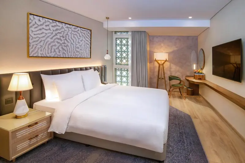 Une chambre lumineuse avec un grand lit et un fauteuil vert.