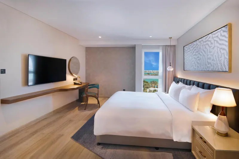 Chambre lumineuse avec un grand lit et un bureau près de la fenêtre.