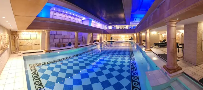 Une piscine intérieure décorée de colonnes et d'un motif à carreaux bleus et blancs.
