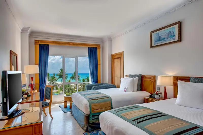 Chambre lumineuse avec deux lits et vue sur la mer.