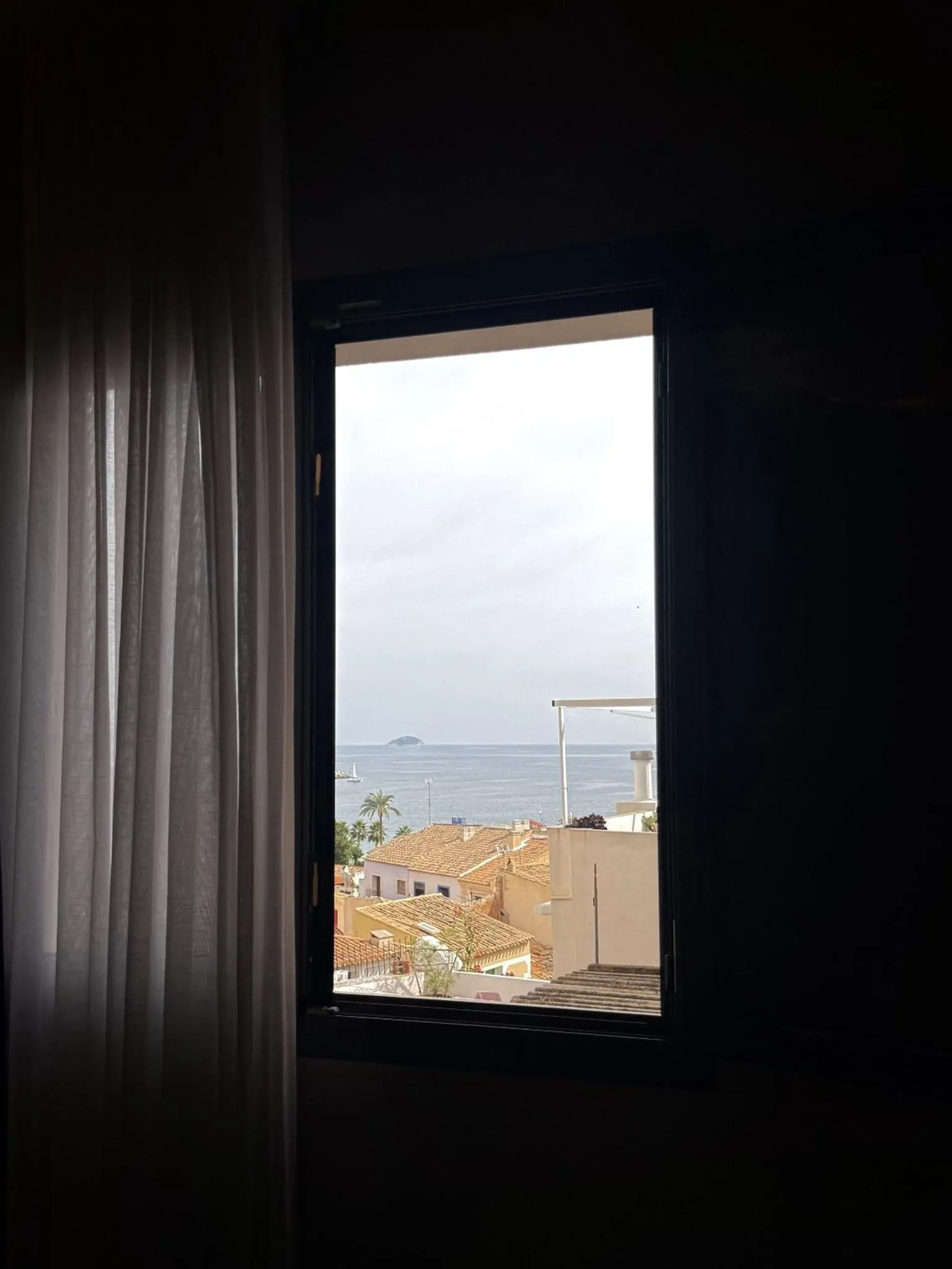 Vue sur la mer depuis une fenêtre avec des rideaux.