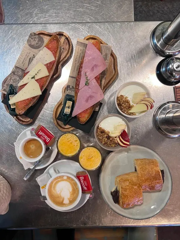 Une table présente un petit-déjeuner avec des tartines, des boissons chaudes et des biscuits.