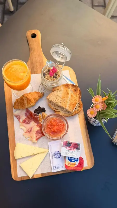 Une planche en bois présente un petit-déjeuner avec des viennoiseries, des fruits et des produits laitiers.