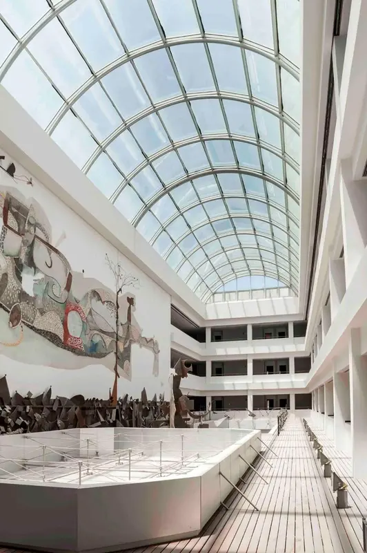 Vaste espace intérieur lumineux avec une verrière et une œuvre d'art murale.