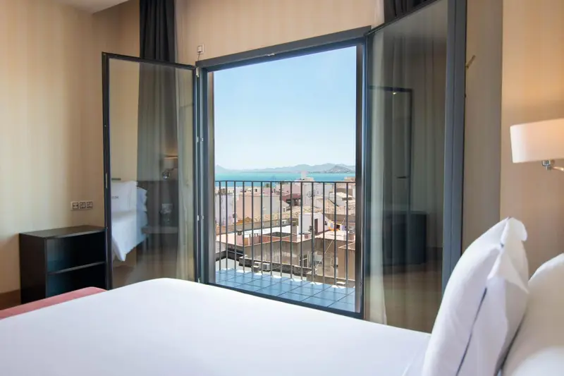 Une chambre d'hôtel lumineuse offre une vue dégagée sur la mer et la ville.