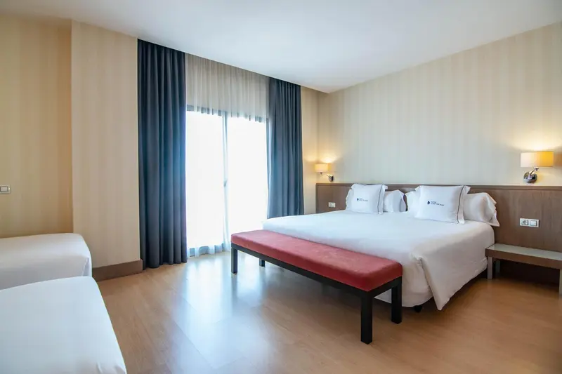 Une chambre lumineuse avec un grand lit et un banc au pied du lit.