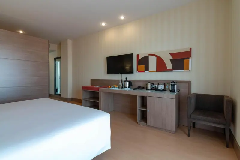 Une chambre lumineuse avec un lit, un bureau et un fauteuil.