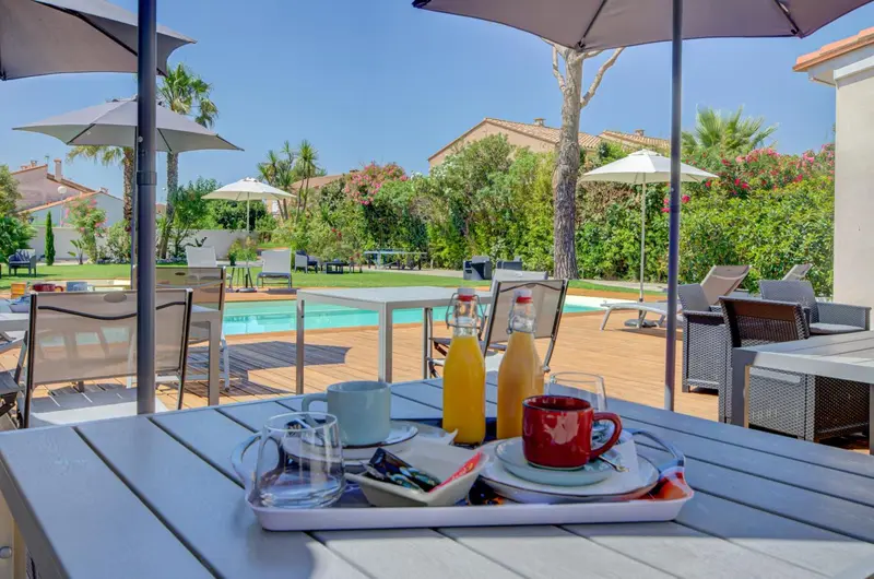 Une table de petit-déjeuner est mise en scène sur une terrasse ensoleillée.
