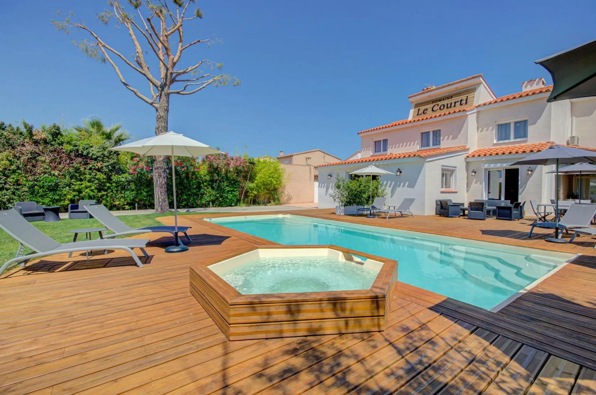 Piscine rectangulaire avec jacuzzi intégré, transats et parasols sur une terrasse en bois.
