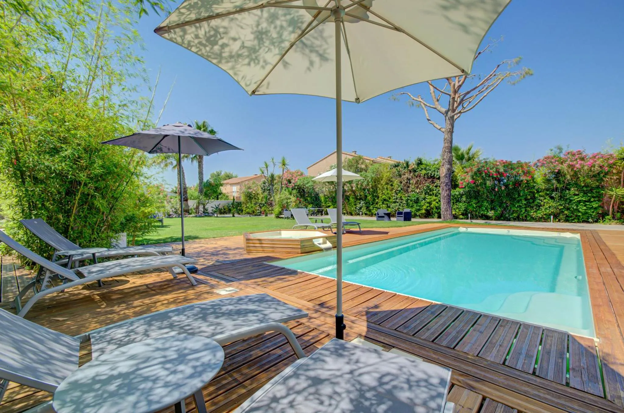 Terrasse avec transats et piscine rectangulaire dans un jardin verdoyant.