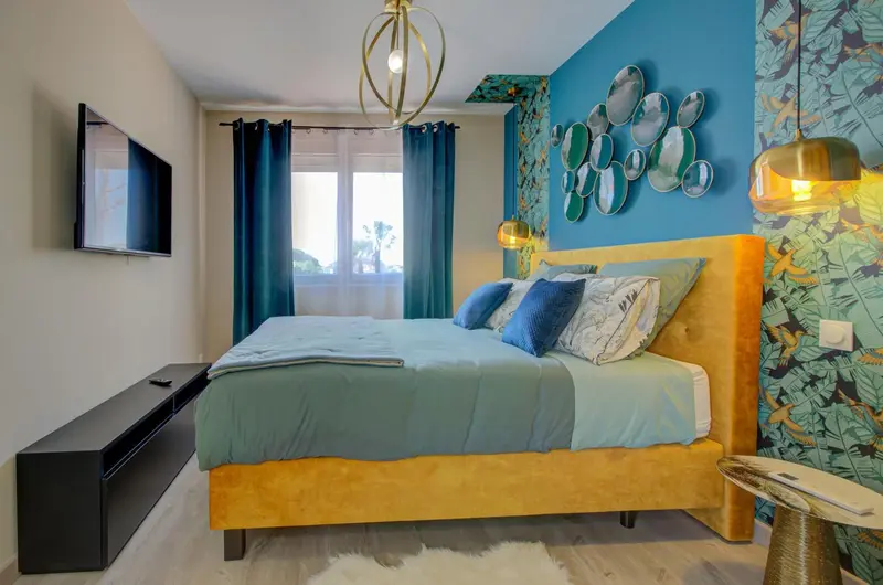 Une chambre lumineuse avec un grand lit recouvert d'une couette turquoise et de coussins.