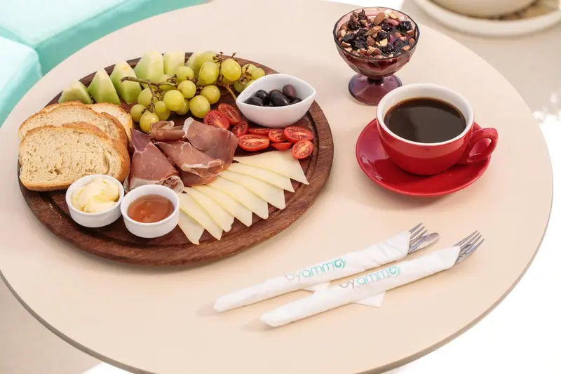 Une table ronde présente une sélection de fruits, de charcuterie, de fromages et de pain.