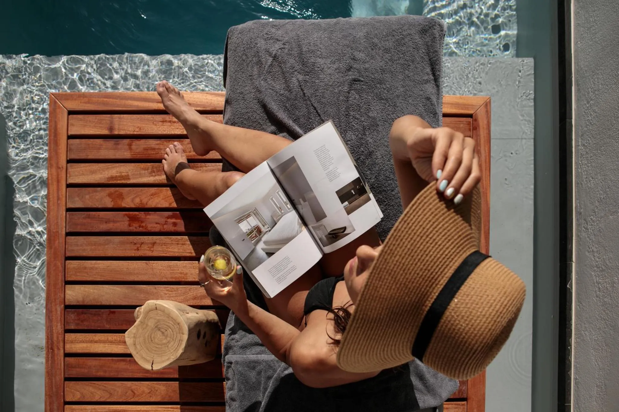 Une personne se relaxe au bord d'une piscine avec un livre et une boisson.