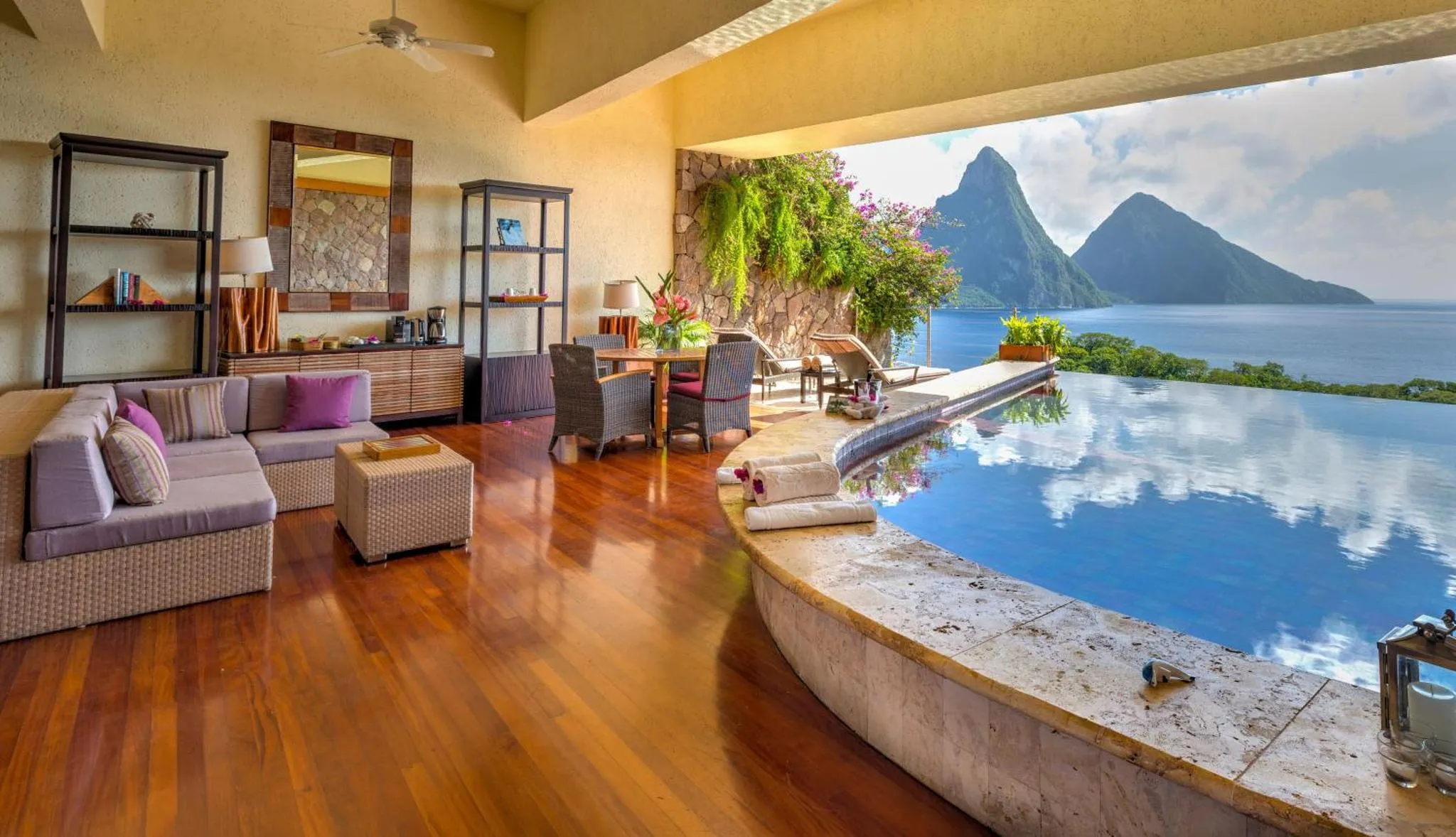 Espace de vie lumineux avec canapé, table et piscine à débordement offrant une vue sur la mer et les montagnes.