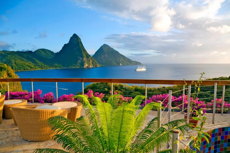 Terrasse fleurie avec mobilier en rotin donnant sur une baie et des montagnes.