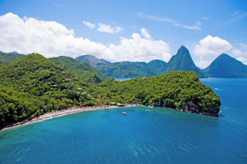 Vue aérienne d'une plage isolée bordée de végétation luxuriante et de montagnes.