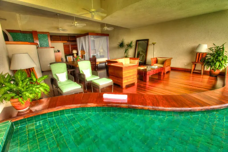 Espace de vie intérieur lumineux avec mobilier en bois et accès à une piscine privée.